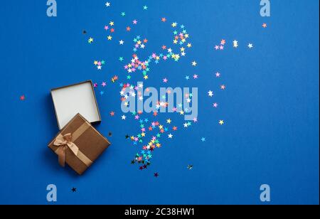 open square empty gift box on a blue background, near multi-colored sequins, top view, festive backdrop Stock Photo