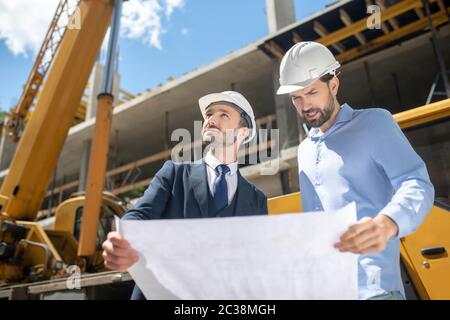 Building site. Building supervisor and foreman standing on the construction site, studying carefully blueprint, checking building process Stock Photo