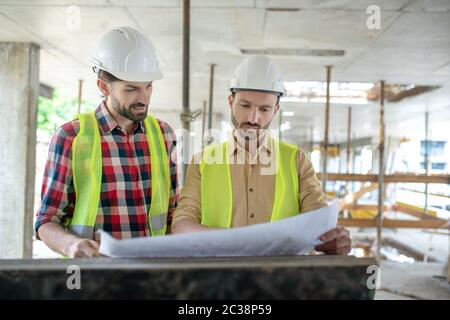 Building site. Building workers brainstorming over blueprint, discussing it Stock Photo
