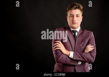 Law student with blond hair dressed in burgundy jacket, white shirt and black tie looking confident posing on isolated black background with copy spac Stock Photo