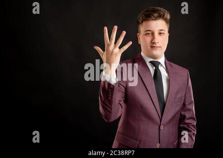 Law student with blond hair dressed in burgundy jacket, white shirt and black tie counting five with his finger posing on isolated black background wi Stock Photo