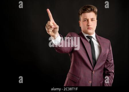 Law student with blond hair dressed in burgundy jacket, white shirt and black tie showing no with his finger posing on isolated black background with Stock Photo