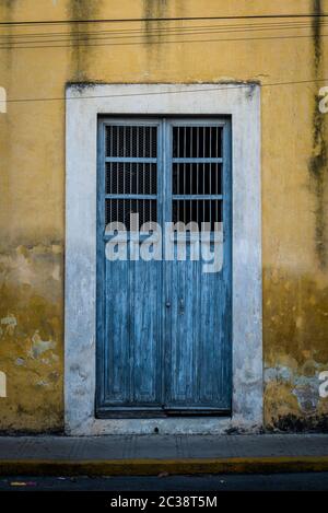 Blue wooden door on a yellow run down facade, Merida, Mexico Stock Photo