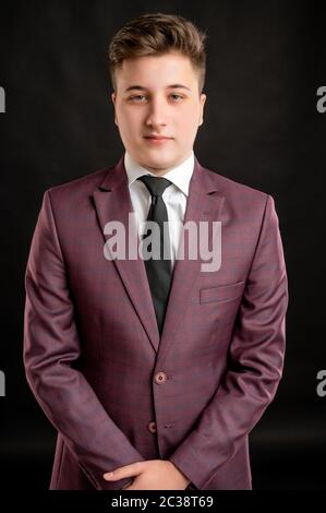 Portrait of law student with blond hair dressed in burgundy jacket, white shirt and black tie posing on isolated lback background with copy space adve Stock Photo