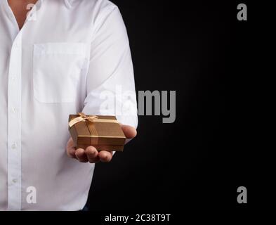 man in a white shirt holds in his left hand a closed little golden box on a dark background, concept proposal of marriage, congratulations on the holi Stock Photo