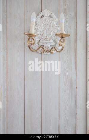 vintage incandescent lamp with iron gold candlesticks hanging on a wooden wall painted white in the room Stock Photo