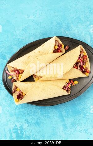 Burritos, sandwich wraps, top-down shot on a vibrant blue background. Mexican tortillas stuffed with ground meat, rice, beans, o Stock Photo
