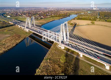 New modern double cable-stayed bridge with wide three-lane roads over Vistula River in Krakow, Poland, and its reflection in water at sunrise. Part of Stock Photo