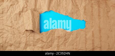 crumpled paper texture from a brown sheet of paper with greasy spots and a large hole with a twisted corner, abstract banner for the designer, blue ba Stock Photo