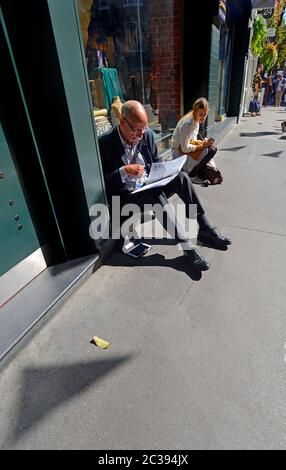 London, England, UK. Man and young woman stitting n the pavement, reading and listening to music Stock Photo