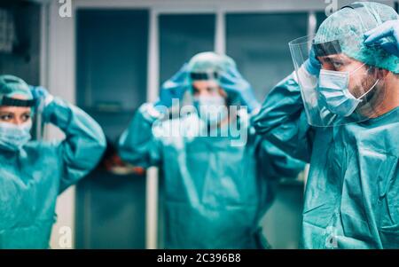 Doctors and nurse preparing to work in hospital for surgical operation during coronavirus pandemic outbreak - Medical workers getting dressed inside c Stock Photo