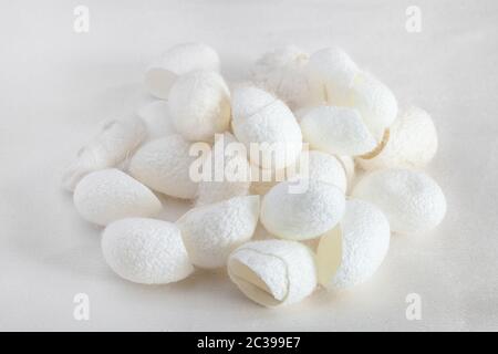 many organic silkworm cocoons for facial skin care on white silk fabric Stock Photo