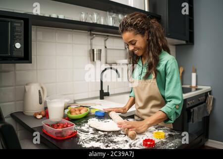 Young african-american woman is making cookies in her kitchen. Stock Photo