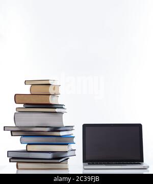E learning concept. Books stack and an open computer laptop with black blank screen isolated on white background. Vertical photo, copy space, template Stock Photo