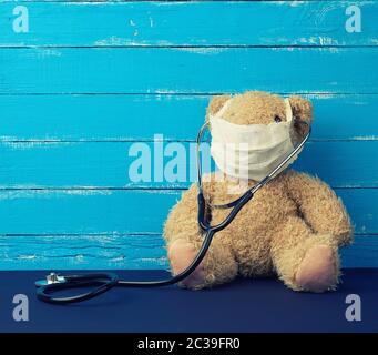 teddy bear is sitting in a white medical mask, black stethoscope is hanging on his neck, a concept for treating children Stock Photo