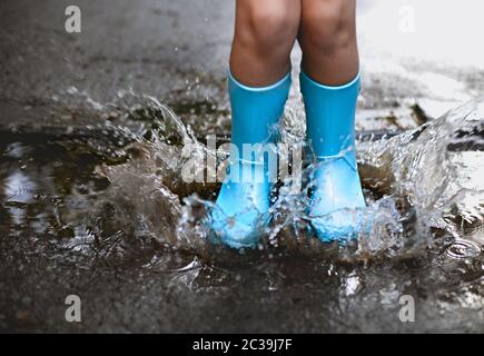 Child wearing blue rain boots jumping into a puddl Stock Photo