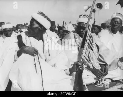Muslim men sit on prayer rugs at the Ramadan festival in Medina, a district of Dakar. A man is holding a rifle. The other men hold prayer chains. Stock Photo