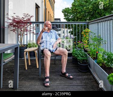 Elderly man sitting on balcony looks thoughtful during Corona Pandemic  in Mitte, Berlin, Germany - Stay at home during COVID-19 Lock-down Stock Photo