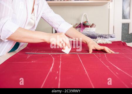 A beautiful seamstress woman in her own atelier makes a pattern on the red fabric. The master is painting the fabric for future clothing. A girl does