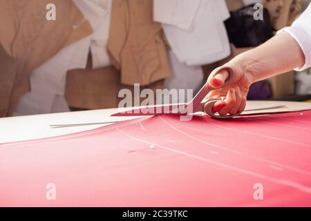 A seamstress woman cuts off the excess red fabric, the girl in the atelier cuts out the details of the pattern for future clothes. The master makes cl Stock Photo