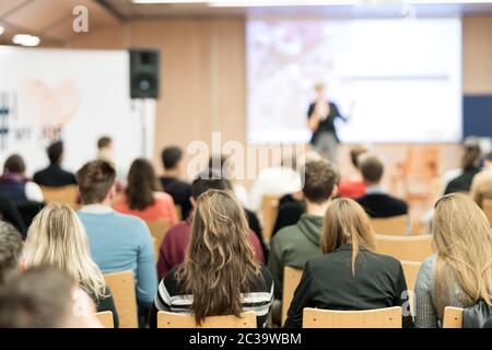 Business and entrepreneurship symposium. Female speaker giving a talk at business meeting. Audience in conference hall. Rear view of unrecognized part Stock Photo