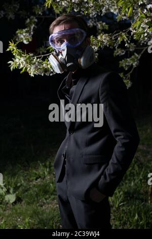 Young man portrait in mask with degree of protection 3M posing in twilight of spring garden. Stock Photo