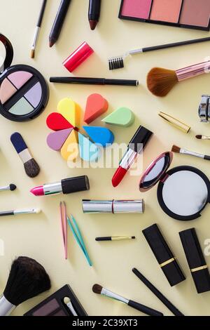 Make up cosmetics flat lay. Lipstick and nail polish, eye shadows and blush, brushes and pencils against yellow color background, top view Stock Photo