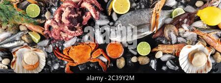 Fish and seafood panorama, a flatlay top shot. Sea bream. shrimps, crab, sardines, squid, octopus and scallops on ice with lemon Stock Photo