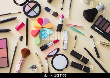 Make up cosmetics flat lay. Lipstick and nail polish, eye shadows and blush, brushes and pencils against yellow color background, top view Stock Photo