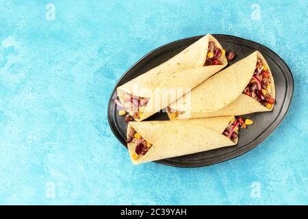 Burritos, sandwich wraps, shot from the top on a blue background. Mexican tortillas stuffed with ground beef meat, rice, beans, Stock Photo