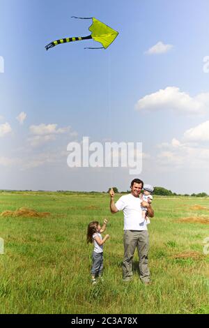 Happy father playing kite with children in meadow in sunny summer day Stock Photo