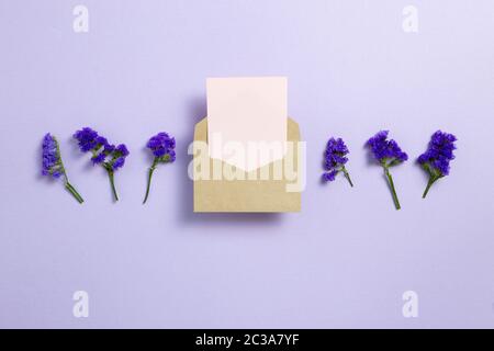 Kraft envelope and empty card with purple statice flowers on light purple background. Floral composition, flat lay, top view, copy space Stock Photo