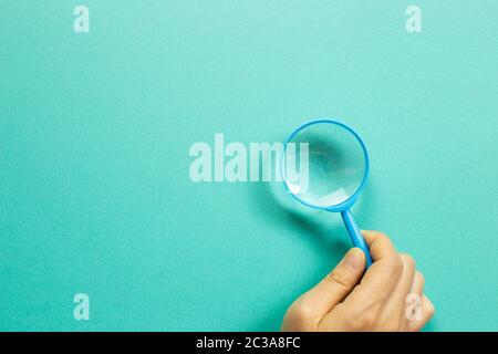 Hand holding a blue magnifying glass on green background. top view, copy space Stock Photo