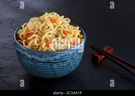 Instant noodles bowl with carrot and scallions, with chopsticks on a black background Stock Photo