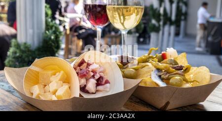 Tapas bar panorama. Cheese, ham and pinchos with red and white wine on a wooden table in an outdoors cafe Stock Photo