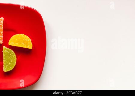 Two Sugar candies. on a red plate. Coloured green, yellow, orange. Shaped as half moon. Plate is placed on a left side. Stock Photo