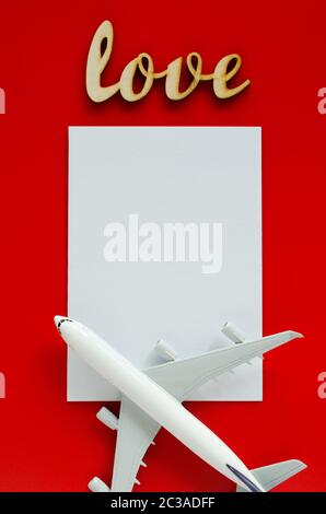 Travel planning on Valentines day . Travel concept, mockup. Blank white paper, inscription love and model of passenger plane on red background. Top vi Stock Photo