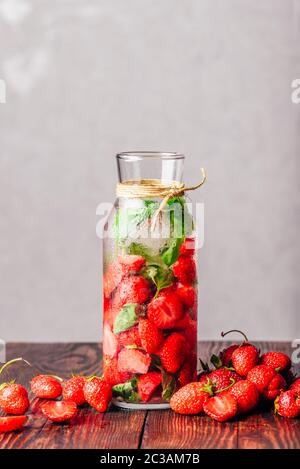 Bottle of Infused Water with Fresh Strawberry and Basil Leaves.Scattered Berries on Wooden Table. Vertical Orientation and Copy Space. Stock Photo