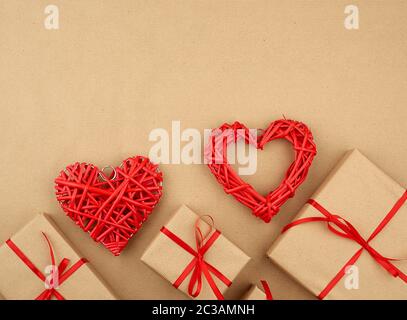 gift wrapped in brown kraft paper and tied with a thin silk ribbon on a background of paper, top view. Congratulations on Valentine's Day February 14, Stock Photo