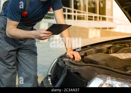 A man in overalls holds clipboard. Mechanic. Car inspection Stock Photo