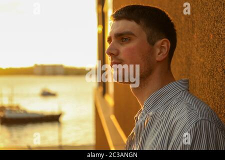 Young man stands leaning against a wall. Amazing sunset Stock Photo