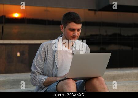 Young man sits in steps and working in laptop outdoor. Freelancer Stock Photo
