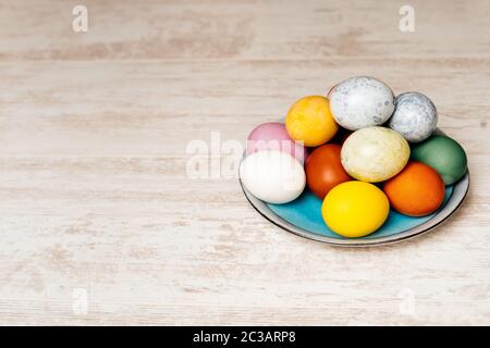 Plate full of multi coloured and mottled Easter eggs. Plate full of eggs on vintage reclaimed oak table or background. Dying Easter eggs. Stock Photo