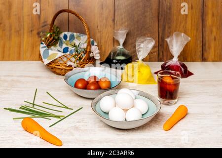 Dying eggs for Easter holiday. White and dyed eggs in decorative bowls and in bags with food colourant nicely arranged on vintage oak wood table Stock Photo