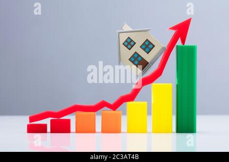 An Increasing Business Graph And Red Arrow Sign With House Model Over Reflective Desk Stock Photo