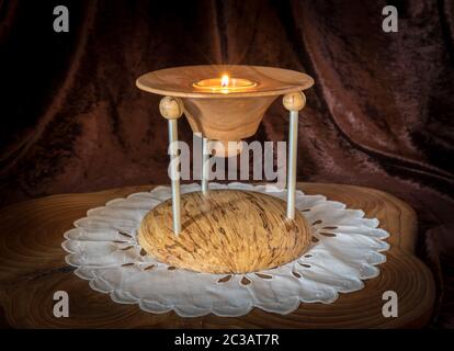 Multi-part wooden candlestick with burning candle stands on a dark wooden board against brown background Stock Photo