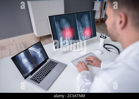 Mature Male Doctor Examining Knee X-ray In Clinic Stock Photo