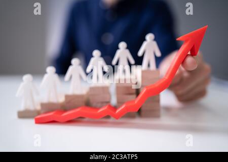 Businessperson's Hand Holding Red Arrow In Front Of Human Figures On Wooden Staircase Stock Photo