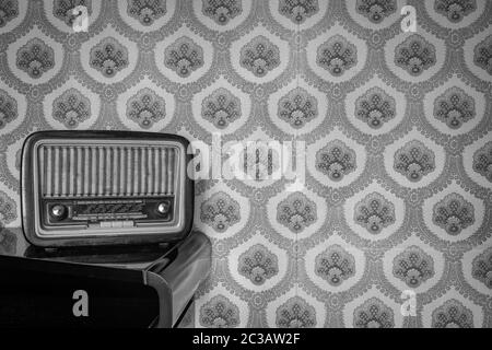 An old transistor radio, with knobs and buttons for manual tuning. In the background a vintage wallpaper. Ancient object, worn and ruined by time. Stock Photo