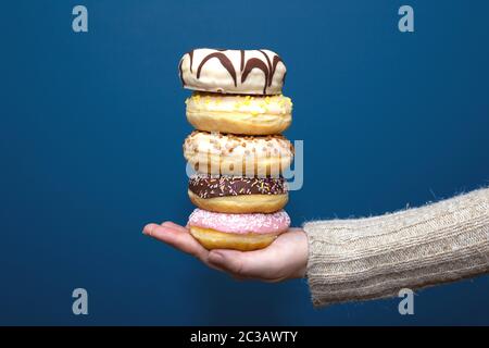 Stack of assorted delicious colorful donuts near dark blue background, sugar concept close-up Stock Photo